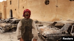 Өртеніп кеткен көліктердің алдында тұрған жергілікті тұрғын. Ливияның шығысындағы Тобрук қаласы, 24 ақпан 2011 жыл