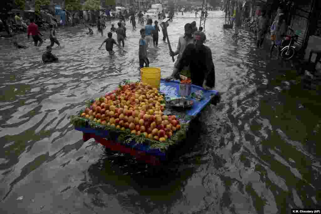 A Pakistani vendor pushes his cart while youngsters play in a flooded street after heavy rainfall in Lahore, Pakistan. (AP/K.M. Chaudary)