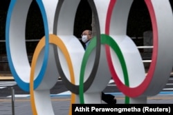 Fotografie din fața Muzeului Olimpic al Japoniei. Un bărbat cu mască de protecție e pozat între cercurile olimpice.