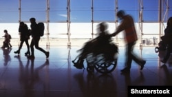 Силуэт человека в инвалидной коляске и людей, перевозящих багаж и идущих в аэропорту
