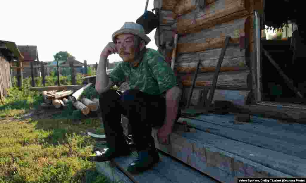 A man sits on the stoop of a traditional wooden home.