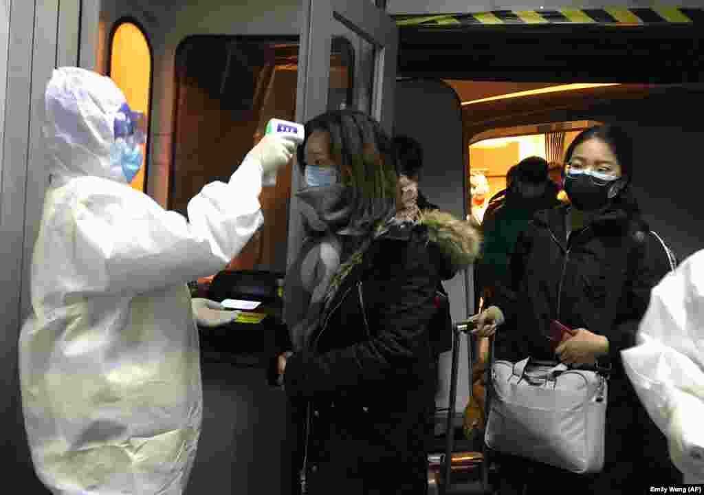 Представники служби охорони здоров’я в спеціальних захисних костюмах перевіряють температуру тіла гостей, які встигли прибути у місто до його закриття на карантин. Фото 22 січня 2020 року
