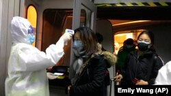 Сотрудник здравоохранения в защитном костюме замеряет температуру тела пассажира, прибывшего из Уханя. Пекин, 22 января 2020 года.