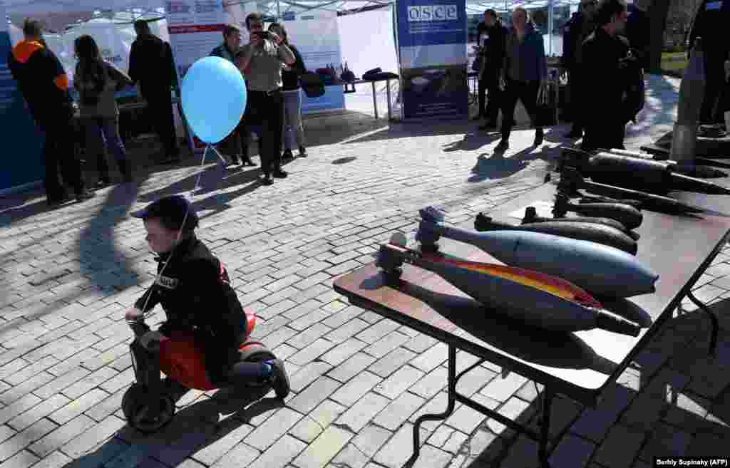 A child rides a scooter past a display of shells during an open-air information day in the center of Kyiv to mark International Mine Awareness Day. More than 1,800 people have been affected by mines and explosive devices in Ukraine and more than 600 of them have died, including children. (AFP/Sergei Supinsky)
