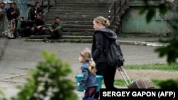 Жінка з дитиною тікає з кварталу, в якому триває бій між прикордонним підрозділом та російськими гібридними силами, які штурмують частину прикордонників у Луганську, 2 червня 2014 року