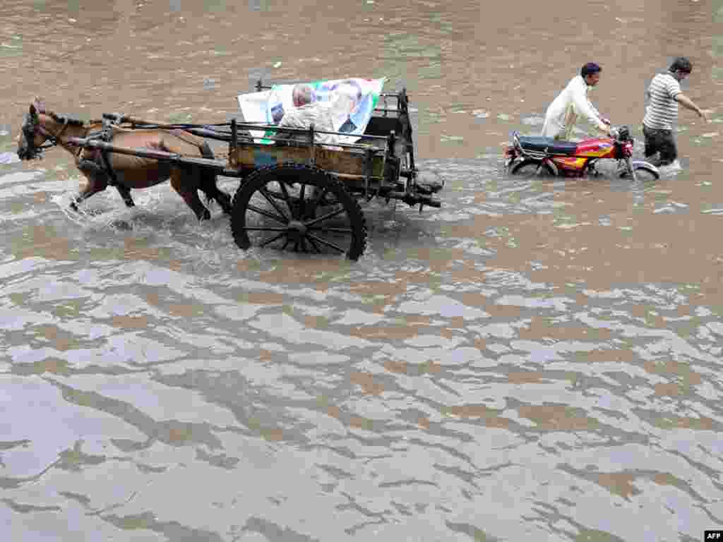 A Pakistani laborer directs his horse-drawn cart past pedestrians wading down a flooded street after heavy monsoon rain in Lahore on July 20.Photo by Arif Ali for AFP