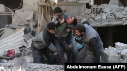 Сирийцы спасают ребенка после воздушного удара сил Асада в повстанческом городе Хамурия, в осажденном регионе Восточная Гута на окраине Дамаска, 21 февраля 2018 года.