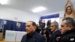 Former Italian Prime Minister leader of Forza Italia party Silvio Berlusconi (left) arrives at a polling station in Milan as a bare-breasted woman from Femen protests in the background on March 4.