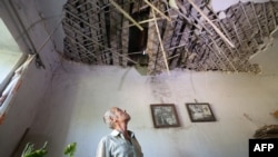 Житель деревни в районе Мариуполя рассматривает крышу своего дома, поврежденную обстрелом