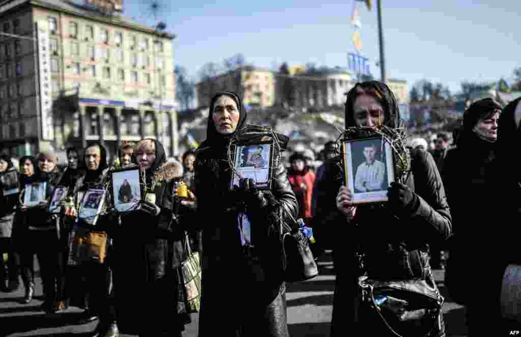 Women hold pictures of protesters who were killed in clashes with police during recent demonstrations as they take part in a commemerative procession in central Kyiv on February 26. (AFP/Bulent Kilic)