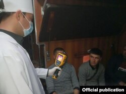 Өзбекстанда пойыз вагонындағы жолаушылардың дене қызуын тексеріп тұрған адам.