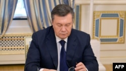 Ukraine - Ukrainian President Viktor Yanukovych looks down at his glasses before signing an agreement in Kiev on February 21, 2014 to end the splintered country's worst crisis