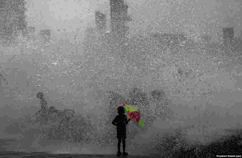 A youngsters holds a colorful umbrella while receiving a soaking after a high wave hit the shoreline during high tide in the Arabian Sea along the promenade in Mumbai, India. (epa/Divyakant Solanki)