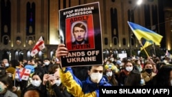 Demonstrators hold up signs and wave flags during a rally in support of Ukraine in Tbilisi on February 28.