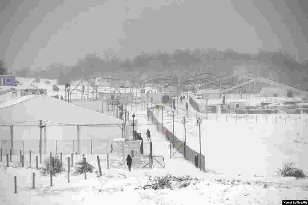 Refugiați mergând prin zăpada care s-a așternut deja peste tabăra arsă de la Lipa, pe 26 decembrie. Tabăra provizorie de corturi de la Lipa a fost deschisă pe 21 aprilie și era destinată doar bărbaților. Potrivit Organizației Internaționale pentru Migrație (OIM), această tabără a găzduit 1359 de migranți.​ &nbsp;