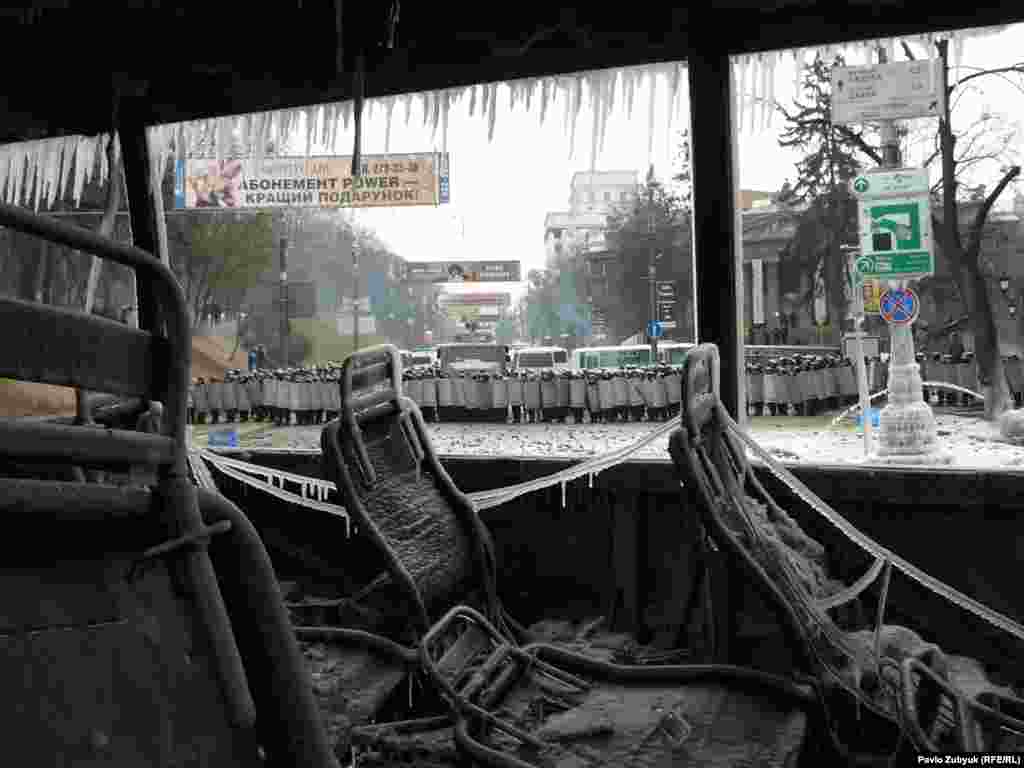 A line of riot police is seen through the shell of a destroyed vehicle.