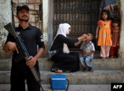 A Pakistani policeman stands guard as a health worker administers the polio vaccine to a child during a vaccination campaign in Karachi, Pakistan, in April. More than 80 polio vaccination team workers in Pakistan have been killed by Taliban militants since a massive polio eradication effort was launched in 2012.