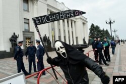 Un protestatar pe a cărui coasă scrie: "Petro, Arseni and Volodimir, plecați".