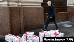 An opposition activist wearing a rubber mask depicting Russian President Vladimir Putin walks past gift boxes reading "Trial," "Resignation," "Impeachment," "True Election," and "Lustration" in Moscow on October 7.