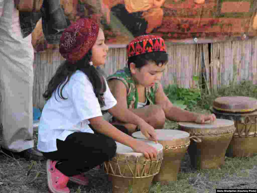 Children wearing traditional Central Asian hats play the drums