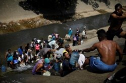 Жители Каракаса, где часто нет электричества и водоснабжения, собирают жидкость из городской сточной канавы