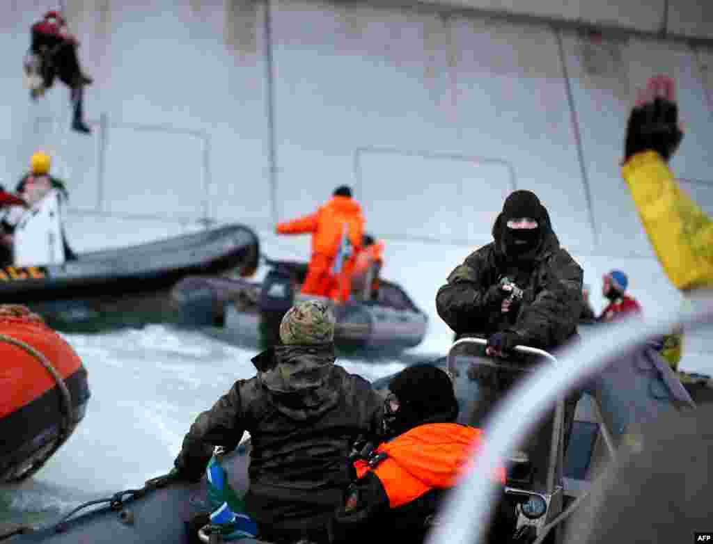 A masked Russian Coast Guard officer points a gun at a Greenpeace International activist (partially visible in lower right corner) during an attempt by environmentalists to climb aboard a Gazprom oil platform in the Pechora Sea in the Russian Arctic. (AFP/Greenpeace/Denis Sinyakov)