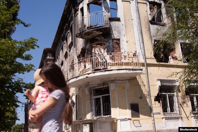 Мама з дитиною біля будівлі в Маріуполі, зруйнованої внаслідок бойових дій