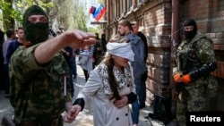 Сепаратист ведет Ирму Крат с завязанными глазами после пресс-конференции в Славянске, 21 апреля 2014 года