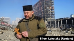 Chaplain Mykola Medinsky holds a cross and a rosary at the site of a military strike on a shopping center in Kyiv on March 21, 2022.