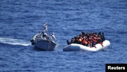 Migrantët qëndrojnë në anijen e tyre të gomës derisa u afrohet ekipi i shpëtimit i Marinës së Italisë 