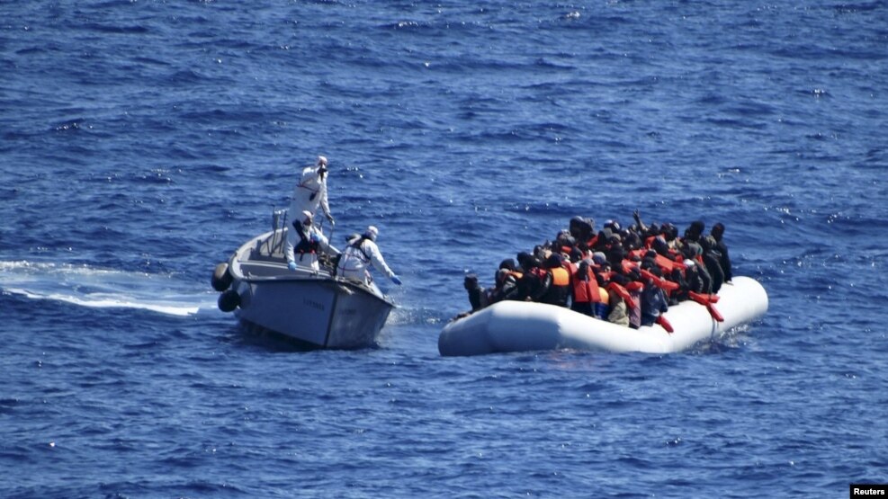 Migrantët qëndrojnë në anijen e tyre të gomës derisa u afrohet ekipi i shpëtimit i Marinës së Italisë 