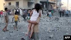 A man carries two children away from the scene of an August 7 explosion in the northern Syrian city of Raqqa. 