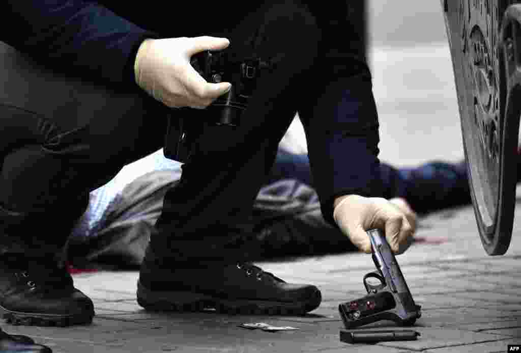 A Ukrainian forensics expert retrieves a gun at the scene where former Russian Duma Deputy Denis Voronenkov, whose body can be seen on the sidewalk behind, was shot dead in the center of Kyiv on March 23. &nbsp;(AFP/Sergei Supinsky)