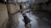 FILE: An Afghan boy gives a thumbs-up as he pushes a wheelbarrow through a muddy lane at a displacement camp in Kabul in November 2019.