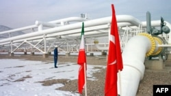 An Iranian worker stands in front of gas pipelines next to the flags of Turkey (R) and Iran