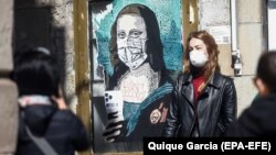 Devojka pozira pored grafita Monalize koja nosi zaštitnu masku