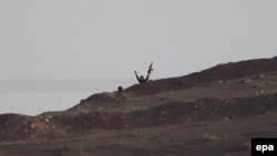 An Islamic State militant waves his hands and gun from a hill near Kobani, in Syria. (file photo)