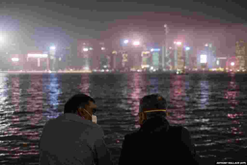 Two men wearing face masks as a precautionary measure against the coronavirus chat while standing near Victoria Harbour in Hong Kong on March 13. (AFP/Anthony Wallace)