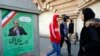 People walk past an electoral poster in a Tehran street, February 13, 2020