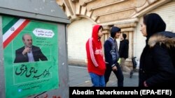 People walk past an electoral poster in a Tehran street, February 13, 2020