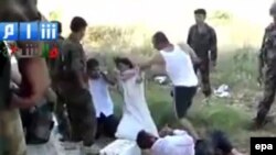 A screen grab from a handout video shows a man dressed in civilian clothes, allegedly belonging to security forces, brutalizing other people dressed in civilian clothes as soldiers in uniform look on in Homs, Syria.