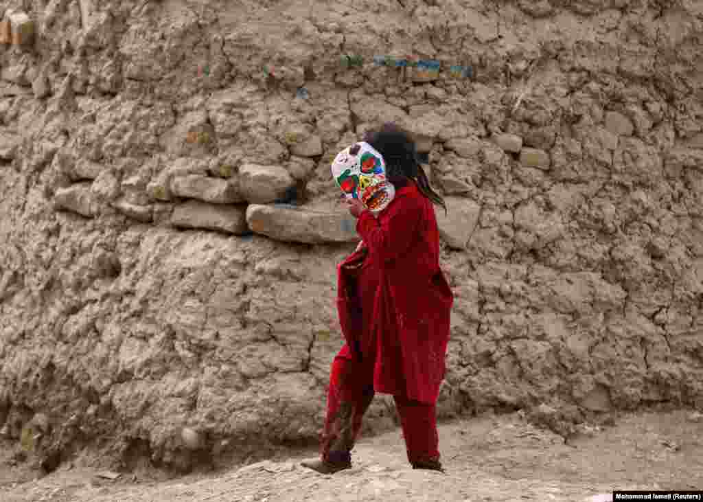 An internally displaced Afghan girl holds a mask as she walks outside a shelter at a refugee camp in Kabul. (Reuters/Mohammad Ismail)