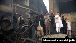 Men take photos with their cellphones at the site of a fire at an electronic appliances market in Kabul on November 2.