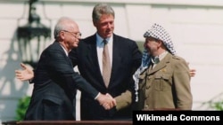 Premierul israelian Yitzhak Rabin și președintele PLO Yasser Arafat dau mâna în fața președintelui american Bill Blinton cu ocazia semnării Acordurilor de la Oslo, 13 septembrie 1993.