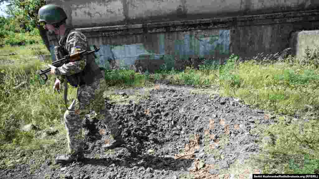 За словами військових, противник веде вогонь із забороненої Мінськими угодами зброї. На фото солдат показує наслідки нещодавнього обстрілу зі зброї калібру понад 120 міліметрів. Снаряд приземлився на розі цивільного будинку