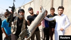 An IS militant (left) stands next to residents as they hold pieces of wreckage from a Syrian war plane after it crashed in Raqqa in September, 2014.