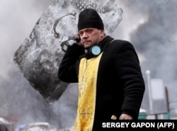 Священник тримає хрест і щит під час зіткнень між учасниками Революції гідності та силовиками в центрі Києва. 20 лютого 2014 року