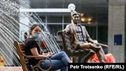 Девушка в защитной маске сидит на скамейке рядом с памятником режиссеру Шакену Айманову. Алматы, 22 июня 2020 года.