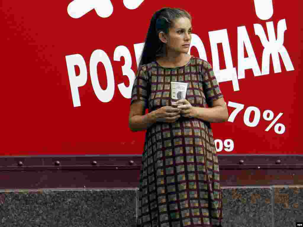 A pregnant woman begs for change on September 14 in front of a store advertisement in Kyiv, Ukraine, one of the countries suffering the effects of the world economic crisis.