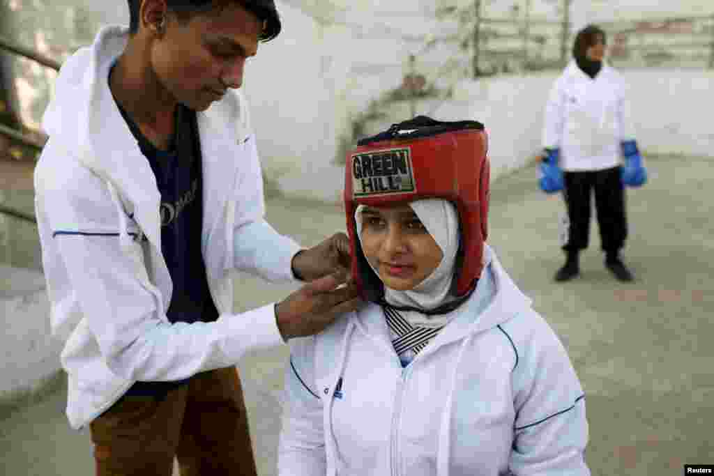 Assistant boxing coach Nadir helps Urooj, 15, put on her headgear before the start of her bout during the Sindh Junior Sports Association Boxing Tournament in Karachi, Pakistan February 21, 2016.&nbsp;